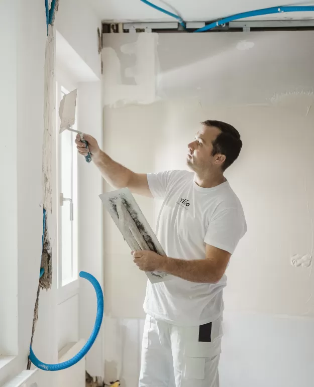 Ein Mitarbeiter der Vilio AG saniert eine weisse Wand.